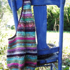 May include: A colorful striped crocheted bag hanging on a blue wooden chair. The bag is made with a variety of different colored yarns, including pink, green, blue, brown, and white.