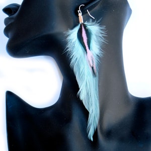 May include: A pair of long, turquoise feather earrings with black and pink accents. The earrings are hanging from a mannequin's ear.