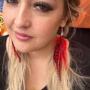 May include: A pair of long red and black feather earrings with silver accents. The earrings are dangling from the woman's ears.