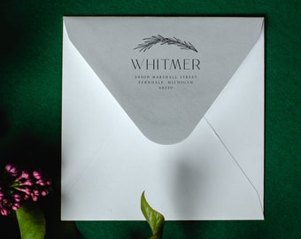 May include: White envelope with a gray interior flap, featuring the name "WHITMER" in a minimalist font, with an illustration of a sprig above the name. Address details are also printed on the flap. The envelope is set against a dark green background.