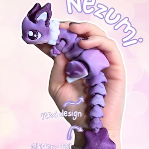 Puede incluir: Una figura articulada de Nezumi morada con una cola de estrella brillante. La figura tiene un diseño flexible y se sostiene en una mano. La figura tiene detalles blancos y la palabra "Nezumi" está escrita en morado.