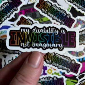 Pode incluir: Um adesivo branco com o texto "My disability is invisible not imaginary" em cores do arco-íris. O adesivo é cercado por outros adesivos com mensagens semelhantes.