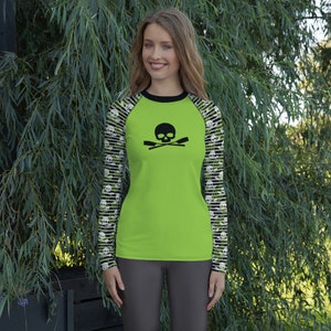 Puede incluir: Una camiseta de manga larga de color verde lima con un diseño negro de calavera y remos cruzados en la parte delantera. Las mangas tienen un patrón de calaveras en blanco y negro.