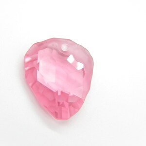 Puede incluir: Un colgante de cristal rosa en forma de coraz&oacute;n con un agujero en la parte superior para enhebrar.
