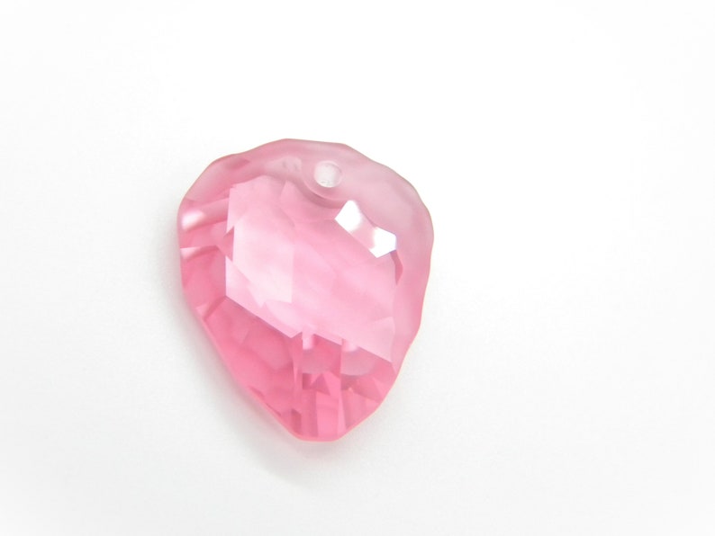 Puede incluir: Un colgante de cristal rosa en forma de coraz&oacute;n con un agujero en la parte superior para enhebrar.