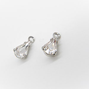 May include: Two silver teardrop-shaped charms with clear crystal accents. The charms have a loop at the top for attaching to jewelry.