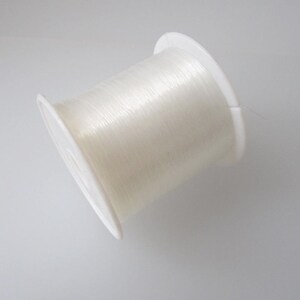 May include: A spool of clear elastic thread wound on a white plastic bobbin.