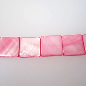 May include: A strand of pink square-shaped shell beads. The beads have a pearlescent finish.