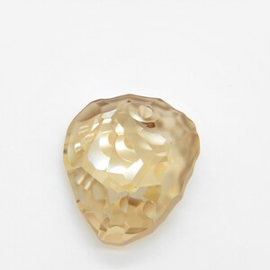 Puede incluir: Un colgante de cristal facetado, transparente y de color dorado, con forma de l&aacute;grima.