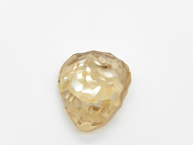 Puede incluir: Un colgante de cristal facetado, transparente y de color dorado, con forma de l&aacute;grima.