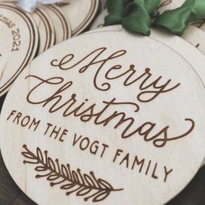 Puede incluir: Un conjunto de adornos redondos de madera con un mensaje grabado con l&aacute;ser que dice "Feliz Navidad de la familia Vogt". Los adornos est&aacute;n decorados con un sencillo dise&ntilde;o de hojas.