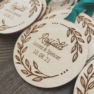 Op de afbeelding: Ronde houten ornamenten met een bladontwerp en de tekst "Raffield Lauren & Spencer 10.08.21" erop gegraveerd.
