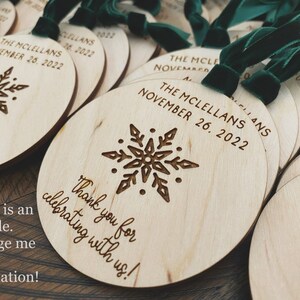 May include: Round wooden ornaments with a snowflake design and the text "The McClellans November 26, 2022" and "Thank you for celebrating with us!" The ornaments have a green velvet ribbon attached.