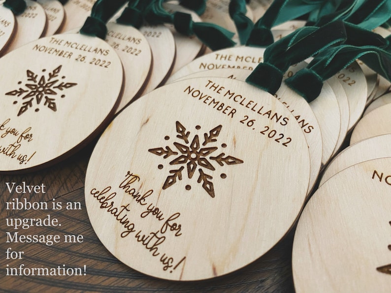 May include: Round wooden ornaments with a snowflake design and the text "The McClellans November 26, 2022" and "Thank you for celebrating with us!" The ornaments have a green velvet ribbon attached.