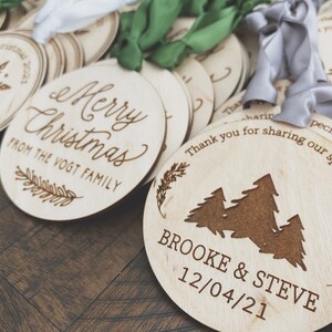 Op de afbeelding: Een verzameling ronde houten ornamenten met lasergegraveerde ontwerpen. Een ornament zegt "Merry Christmas from the Vogt Family". Een ander ornament heeft een ontwerp van drie dennenbomen en zegt "Brooke & Steve 12/04/21".