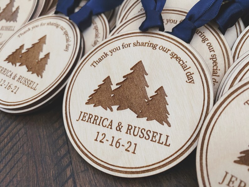 Op de afbeelding: Ronde houten ornamenten met een lasergegraveerd ontwerp van drie dennenbomen en de tekst "Bedankt voor het delen van onze speciale dag" en "Jerrica & Russell 12-16-21".