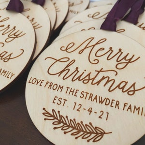 Puede incluir: Un conjunto de adornos redondos de madera con el texto "Merry Christmas" y "Love from the Strawder Family Est. 12-4-21" grabado en ellos. Los adornos son de color marr&oacute;n claro y tienen un aspecto r&uacute;stico y hecho a mano.