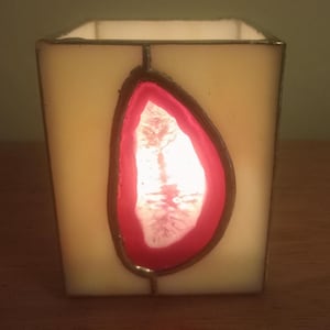 May include: A square glass candle holder with a pink agate design. The candle holder is lit and the light shines through the agate.