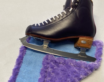 May include: Purple figure skate with white laces and a silver blade. The skate is resting on a light blue and purple fuzzy mat with the word "Phantom" printed on the blade.