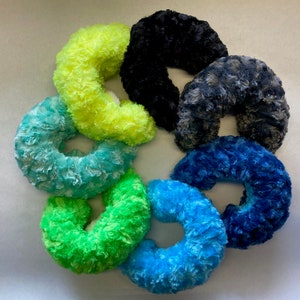 May include: Six plush neck pillows in a variety of colors, including black, gray, blue, green, and yellow. The pillows are arranged in a circle, with the opening of each pillow facing outwards.