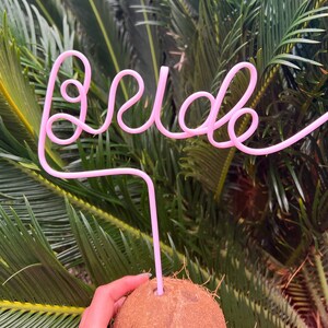 May include: A pink plastic straw bent into the word "bride" with a coconut underneath.