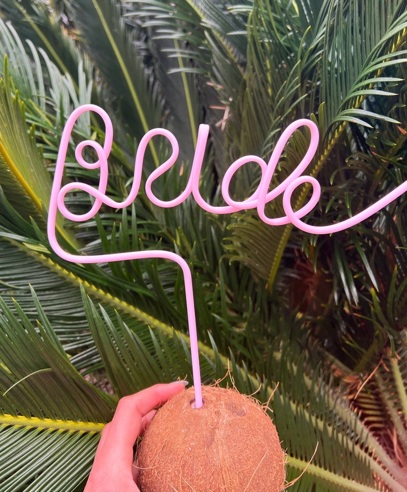 May include: A pink plastic straw bent into the word "bride" with a coconut underneath.