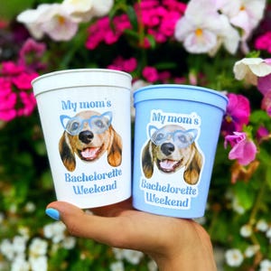 Peut inclure: Un gobelet en plastique blanc et un gobelet en plastique bleu clair, chacun orn&eacute; d'un graphique repr&eacute;sentant un chien portant des lunettes bleues et le texte "My mom's Bachelorette Weekend" imprim&eacute; en bleu sur le devant.