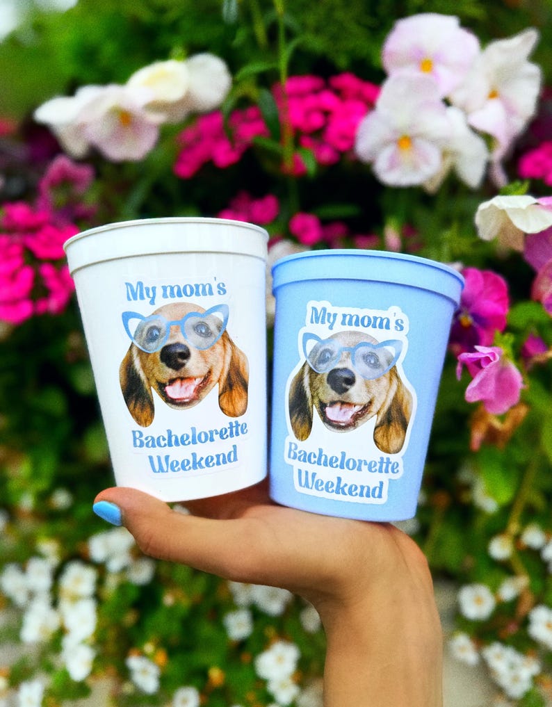 Peut inclure: Un gobelet en plastique blanc et un gobelet en plastique bleu clair, chacun orn&eacute; d'un graphique repr&eacute;sentant un chien portant des lunettes bleues et le texte "My mom's Bachelorette Weekend" imprim&eacute; en bleu sur le devant.