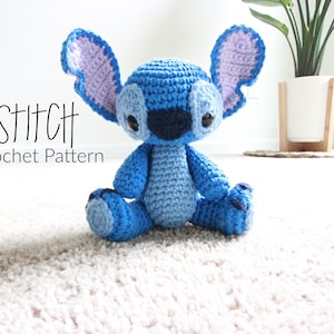 May include: A blue and purple crocheted Stitch plush toy from the Disney movie Lilo & Stitch. The toy is sitting on a white carpet. The text "STITCH Crochet Pattern" is visible in the image.