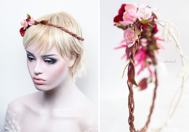 May include: A floral headband featuring a braided brown vine-like band adorned with artificial pink and deep red flowers and green leaves. The accessory is displayed on a mannequin head, showcasing the intricate twisted texture of the band.