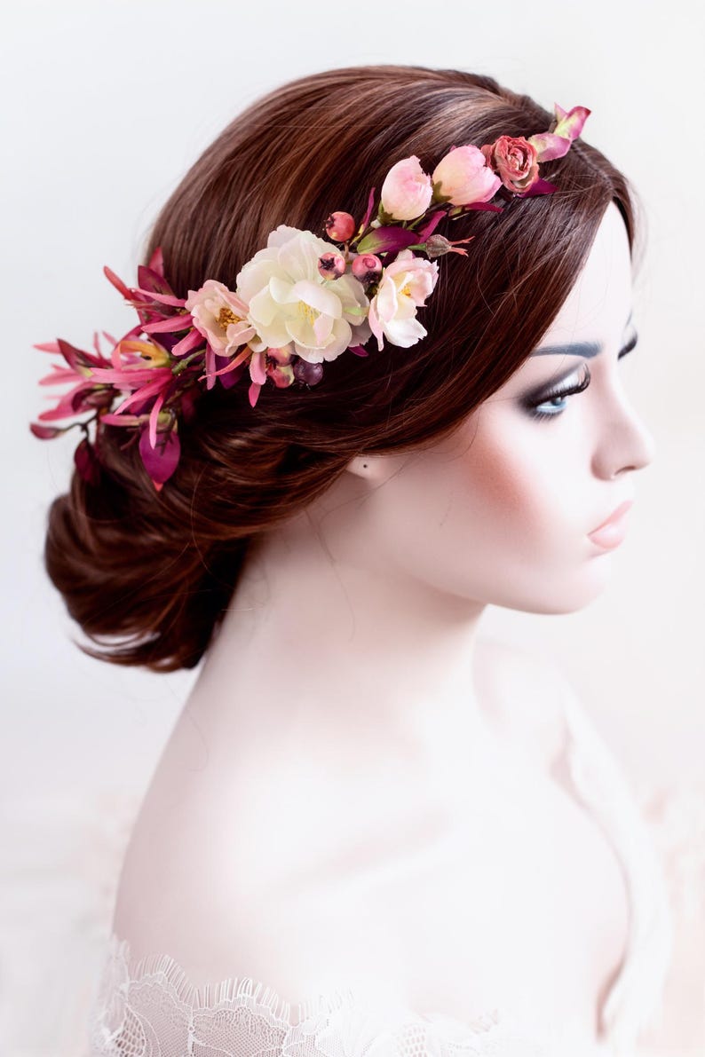 May include: A floral hair crown featuring an arrangement of cream-colored roses, small pink buds, and deep magenta-colored foliage. The accessory is positioned across the top of the head, showcasing a mix of soft pastel and vibrant berry tones.