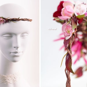 May include: A floral crown featuring a twisted brown vine base adorned with pink, white, and deep red artificial flowers and green leaves. The accessory is displayed on a white mannequin head, showcasing a detailed arrangement of blossoms and foliage.
