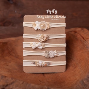 May include: Five nude nylon headbands with different floral and pearl embellishments displayed on a brown card with the text "Baby Little Miracle Photo Props".