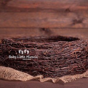 Könnte beinhalten: Ein braunes Zweig-Nest, aus natürlichen Zweigen geflochten, liegt auf einem Jutestoff. Das Nest ist ein beliebtes Accessoire für Neugeborenenfotografie.