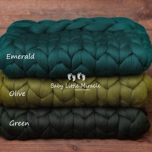 May include: Three chunky knit blankets in shades of green, stacked on top of each other. The top blanket is emerald green, the middle blanket is olive green, and the bottom blanket is a darker shade of green. The blankets are labeled "Emerald", "Olive", and "Green". The text "Baby Little Miracle Photo Props" is also visible on the blankets.
