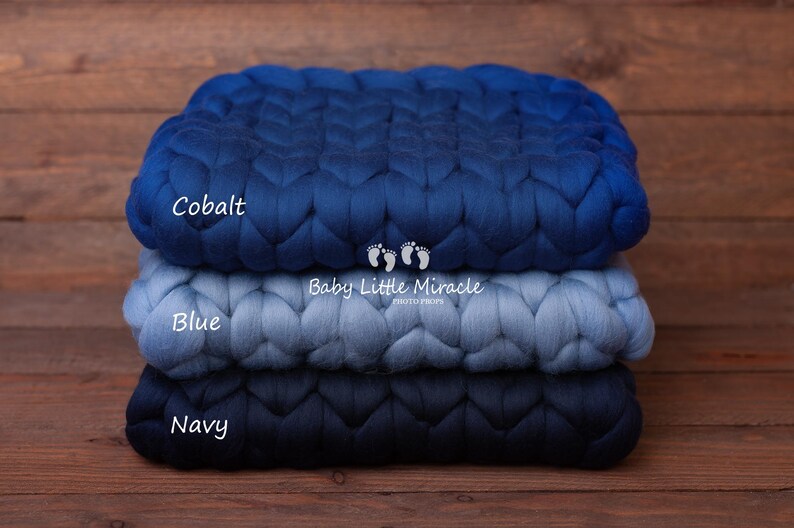 May include: Three knitted blankets stacked on top of each other. The top blanket is cobalt blue, the middle blanket is blue, and the bottom blanket is navy blue. The blankets are made of chunky yarn and have a braided texture. The text "Cobalt", "Blue", and "Navy" is written on each blanket. The text "Baby Little Miracle" is written on the middle blanket.