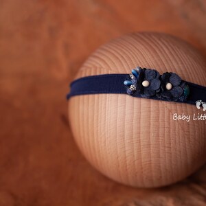 May include: A navy blue headband with a blue and white flower embellishment. The headband is on a wooden surface. Baby Little Miracle Photo Props.