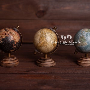 Pode incluir: Três globos em miniatura com estilo antigo estão sobre uma superfície de madeira escura. Os globos apresentam diferentes esquemas de cores: preto e castanho, bege e azul e verde. Cada globo é montado numa base de madeira com uma estrutura metálica cor de latão.