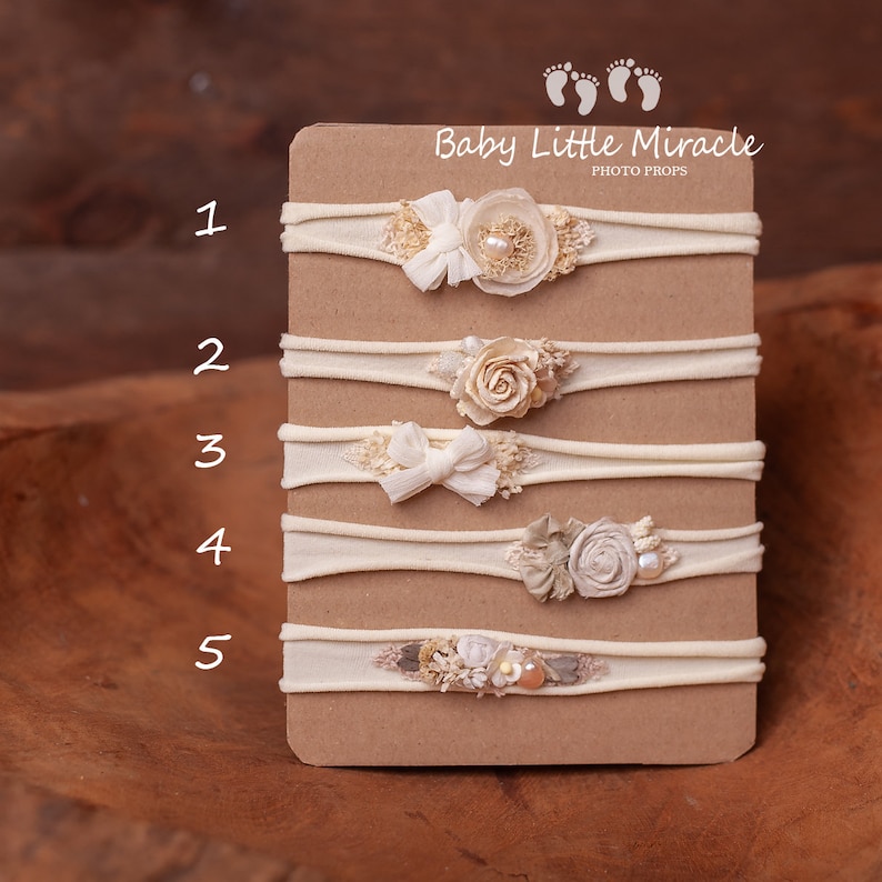 May include: Five white elastic headbands with different floral and pearl embellishments. The headbands are numbered 1 through 5 on a beige card with the text "Baby Little Miracle Photo Props".
