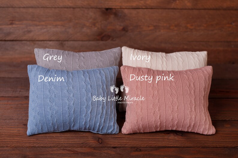 Puede incluir: Cuatro almohadas rectangulares de punto en gris, denim, marfil y rosa empolvado. Cada almohada presenta un dise&ntilde;o de punto trenzado. Las almohadas est&aacute;n dispuestas sobre una superficie de madera oscura. Los textos "Grey", "Denim", "Ivory" y "Dusty pink" est&aacute;n escritos en las almohadas.