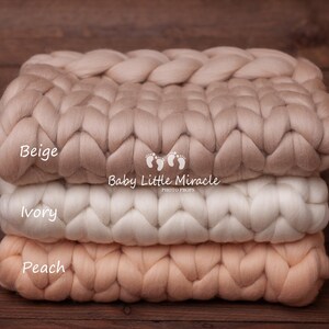 May include: Three chunky knit blankets stacked on top of each other. The top blanket is beige, the middle blanket is ivory, and the bottom blanket is peach. The blankets are made of thick, soft yarn and have a woven texture.