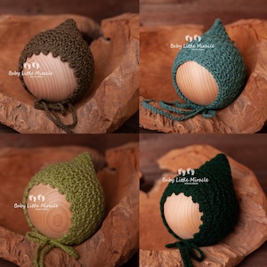 Peut inclure: Quatre bonnets en crochet pour bébé dans différentes nuances de vert. Les bonnets sont présentés sur une surface en bois. Les bonnets ont un sommet pointu et une cravate.