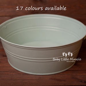 Peut inclure: Une cuve en métal gris clair avec deux poignées, idéale pour la photographie de bébé. La cuve a une forme arrondie avec des rainures horizontales. Le texte "17 couleurs disponibles" est en haut. Le logo "Baby Little Miracle PHOTO PROPS" est sur le côté.