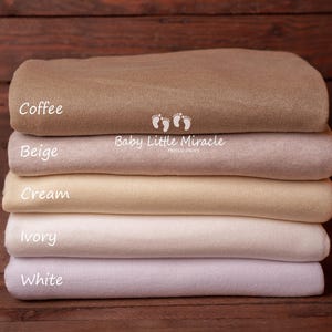 K&ouml;nnte beinhalten: Ein Stapel von sechs gefalteten Decken in den Farbt&ouml;nen Braun, Beige, Creme, Elfenbein und Wei&szlig;. Die oberste Decke ist mit "Coffee" beschriftet, die anderen mit "Beige", "Cream", "Ivory" und "White". Die Decken sind f&uuml;r Neugeborene.