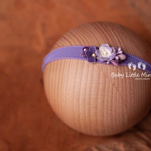May include: Purple headband with a flower embellishment. The headband is made of a soft, stretchy material and is perfect for newborn photography.