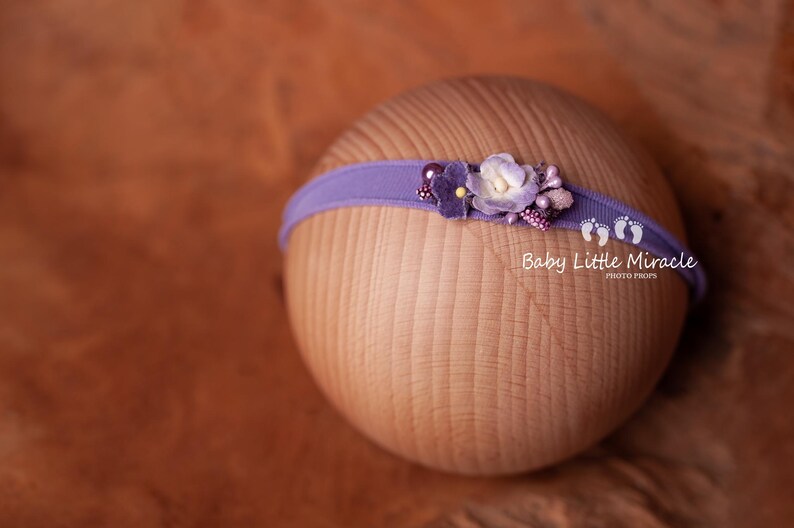 May include: Purple headband with a flower embellishment. The headband is made of a soft, stretchy material and is perfect for newborn photography.