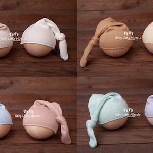 K&ouml;nnte beinhalten: Sechs Neugeborenen-M&uuml;tzen in verschiedenen Farben: Beige, Wei&szlig;, Hellbraun, Creme, Hellblau, Rosa, Mintgr&uuml;n und Lavendel. Jede M&uuml;tze ist am Ende geknotet und sitzt auf einem Holz-Requisit.