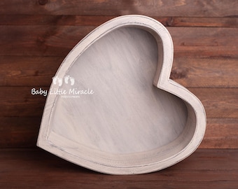 May include: A heart-shaped wooden bowl with a distressed, whitewashed finish. The interior and exterior surfaces show visible wood grain texture. The text Baby Little Miracle Photo Props is printed in white on the left side of the bowl.