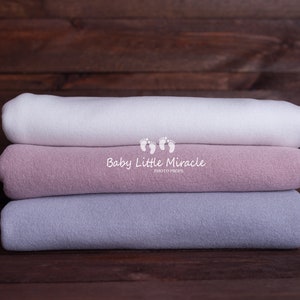 Può includere: Tre fasce di stoffa impilate l'una sull'altra. La fascia superiore è bianca, la fascia centrale è rosa chiaro e la fascia inferiore è grigio chiaro. Il testo "Baby Little Miracle Photo Props" è stampato sulla fascia centrale.