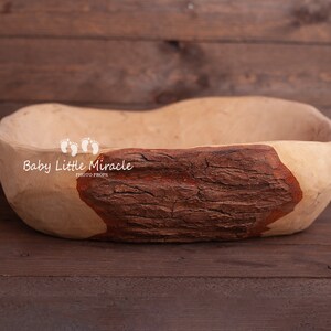 May include: A large, wooden bowl with a natural brown finish. The bowl has a rough, textured surface and a dark brown patch on one side. The bowl is ideal for newborn photography props.